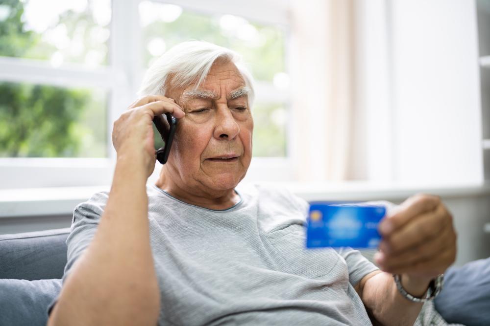 En gråhårig man talar i mobiltelefon och har ett bankkort i andra handen. 