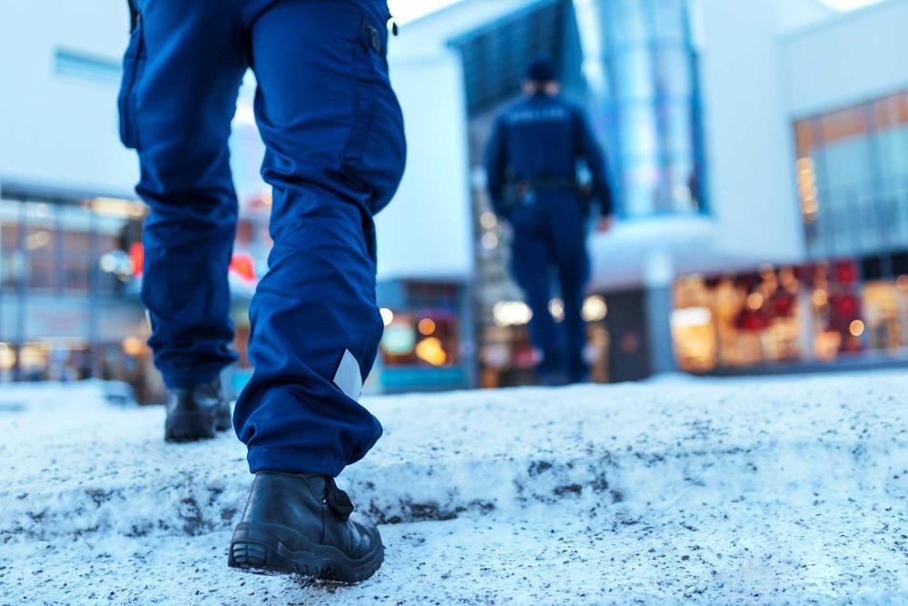 En polispatrull promenerar mot ett köpcentrum, man ser ryggen av konstapeln som går före, medan den andra konstapeln syns i förgrunden.