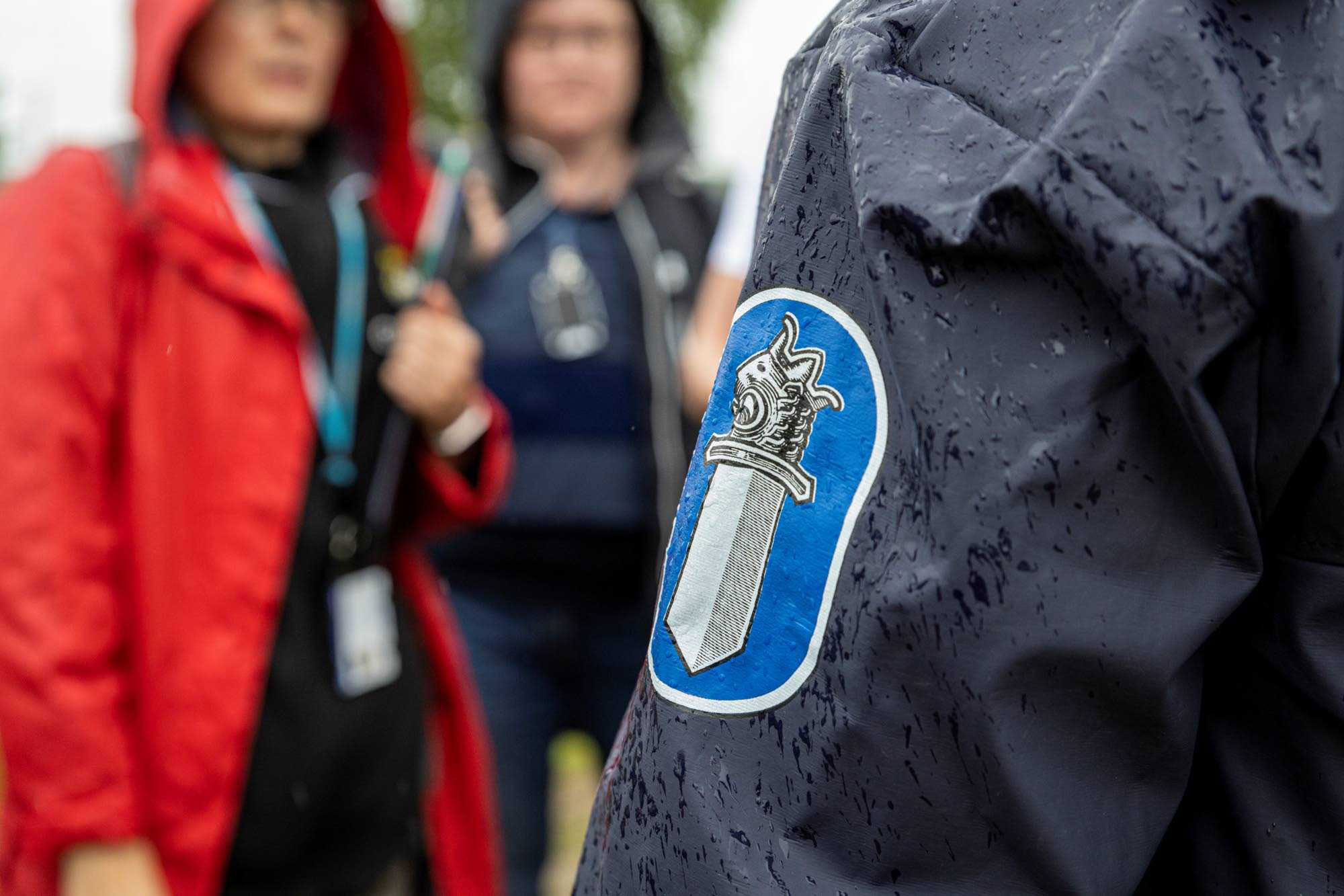 Två poliser diskuterar med en representant för räddningsmyndigheten. I förgrunden ryggsidan på en polis i regnrock. 