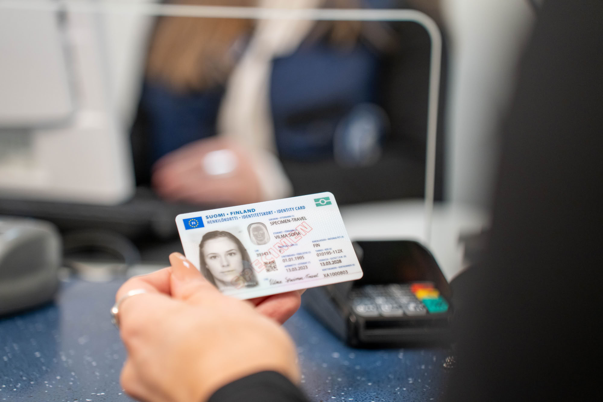 En kund håller ett identitetskort i handen. I bakgrunden syns en tillståndssekreterare.