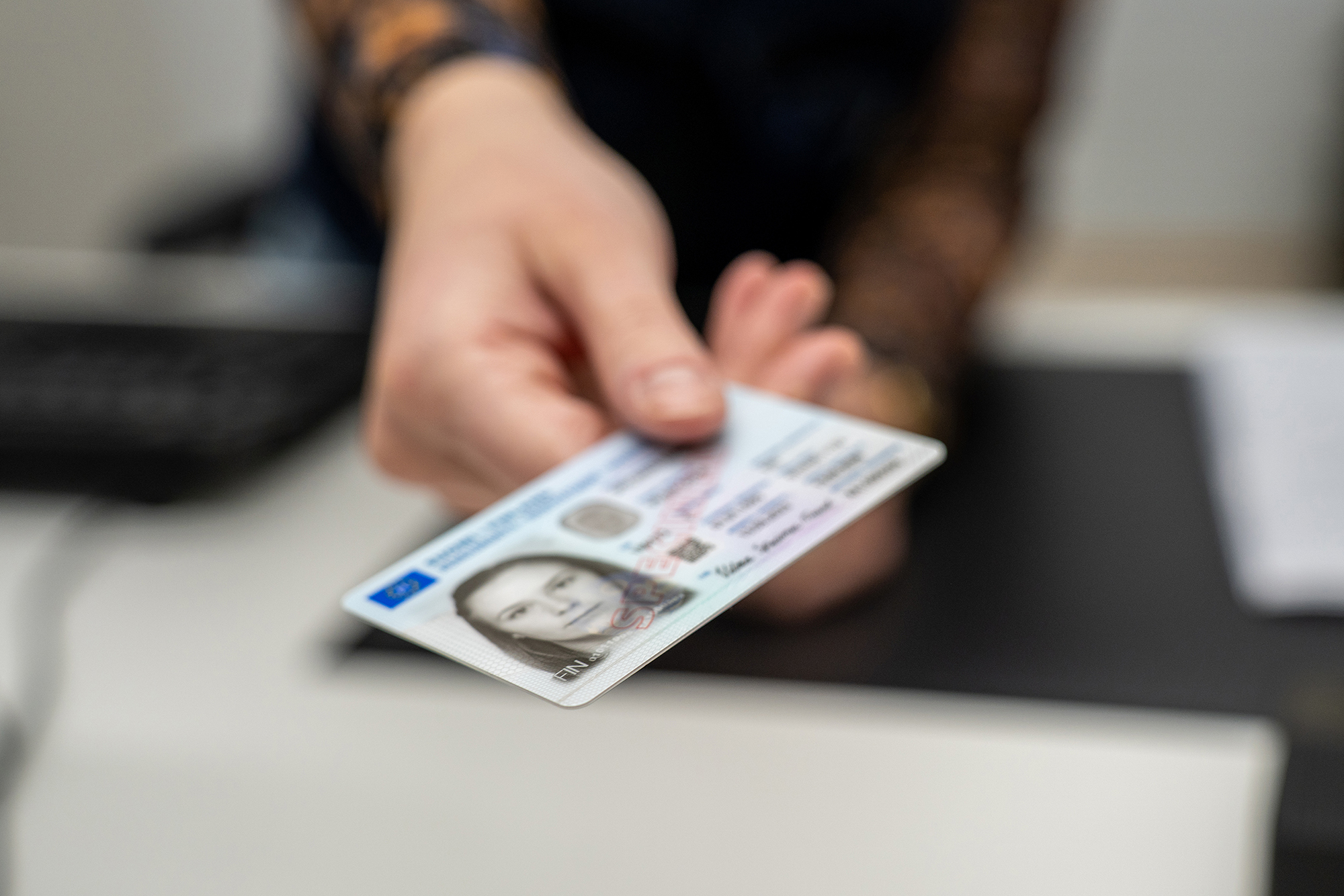 Tillståndssekreterarens hand räcker över ett identitetskort till en kund.