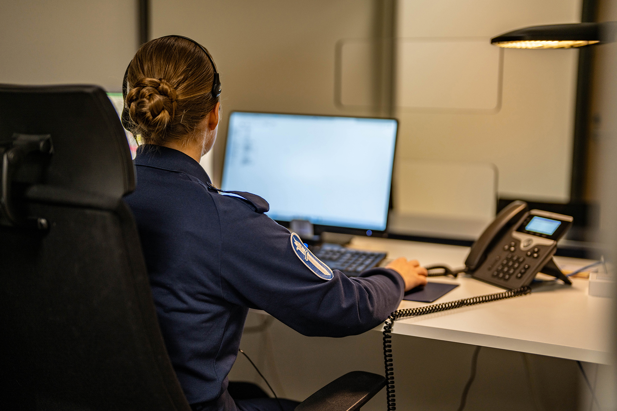 En polis arbetar vid en dator och registrerar en brottsanmälan, med en kundtjänstdisk i bakgrunden.