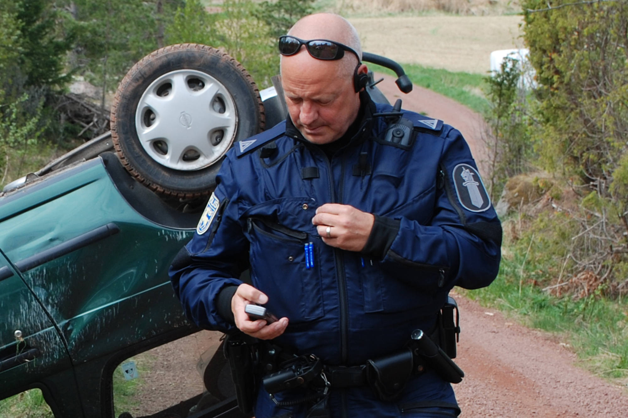 Uniformerad polisman går från en fordonsolycksplats och tittar på sin mobiltelefon.
